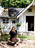 Kleines Mädchen auf Schaukel aus Weidenzweigen, im Hintergrund weisses Holzhaus