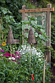 Gartenstecker mit Hütchen aus Geflecht zwischen blühenden Stauden