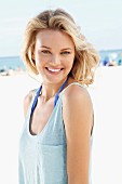 A young blonde woman on a beach wearing a blue tank top