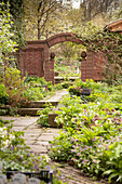 Angelegte Beete in idyllischem Garten, im Hintergrund Ziegelmauer mit integriertem Torbogen