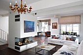 Open-plan interior with white sofas in front of open fireplace below blue modern artwork on free-standing chimney breast