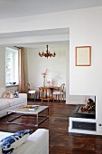 Coffee table in front of fireplace; dining area with chandelier and antique furnishings in background