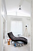 Charcoal grey, button-tufted lounger, stool used as side table and books on floor in white, purist interior