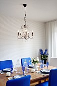 Kristallleuchter über gedecktem Tisch mit königsblau gepolsterten Stühlen und Rittersporn im Hintergrund
