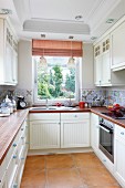 Modern, U-shaped fitted kitchen in country-house style with mixture of tiles on splashback, wooden worksurfaces and red and white striped roller blinds