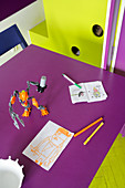 Kinderzeichnungen und Spielzeugfigur auf der violetter Tischplatte, angrenzendes Einbaumöbel und Boden in komplementärem Lindgrün