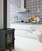 Blue and white Moroccan wall tiles above modern, elegant kitchen counter with wide drawers; wood-burning stove in foreground