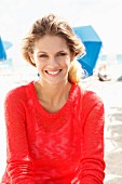 A young blonde woman on a beach wearing a transparent red knitted jumper