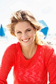 A young blonde woman on a beach wearing a transparent red knitted jumper