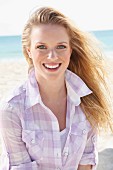 A young blonde woman on the beach wearing a purple and white checked blouse