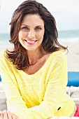 A brunette woman on a beach wearing a yellow knitted jumper
