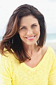 A brunette woman on a beach wearing a yellow knitted jumper