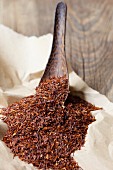 Rooibos tea leaves on a wooden spoon and on paper