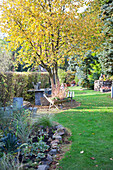 Small flowerbeds and seating area under trees and sculptures on plinths in summery garden