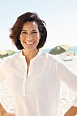 A brunette woman on a beach wearing a thin white blouse