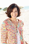 A brunette woman on a beach wearing a white top and colourful cardigan