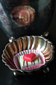 A praline decorated with a heart in a silver dish