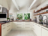 White, modern, fitted kitchen in renovated country house with crockery on wooden shelves, worksurfaces and exposed, white roof beams