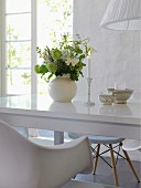 Zart romantische Tischdekoration mit Kerzenlicht und Blumenstrauß auf glänzender weißer Tischplatte, geöffnete Terrassentür