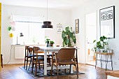 Retro chairs with wooden frames around white dining table below pendant lamp in front of house plants next to window