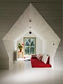 Wood-clad niche in converted attic; red futon and cushions on white-painted wooden floor