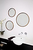 Trio of mirrors made from old round picture frames above modern sink with taps mounted on white mosaic wall tiles
