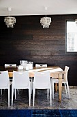 Stacking chairs, large wooden table, crystal chandelier, dark wooden wall and royal blue rug on travertine floor in dining room
