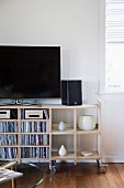 TV, speakers, CDs and vases on open-fronted vintage shelving on castors