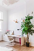 White desk, vintage rocking chair, green tree and faux hunting trophies in bright child's bedroom