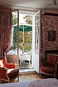 Antique armchairs flanking open French windows leading to seating area on balcony