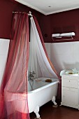 Free-standing, clawfoot bathtub under red and white fabric canopy