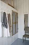 Wandhakenleiste mit aufgehängten Handtüchern neben Einbauschrank mit rustikalen Holzlamellentüren, als Raumteiler mit weisser Holzverschalung