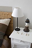 Minimalist table lamps with white lampshade on white-painted bedside cabinet with stencilled lettering