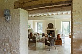 Blick durch Durchgang in renoviertes Wohnzimmer eines mediterranen Landhauses, Rattanstühle und Sofa vor Kamin