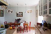 Dining area with red-painted kitchen chairs below row of pendant lamps in rustic kitchen