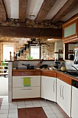 Offene Küche mit auskragender Küchenzeile und Thekenaufsatz, im Hintergrund Treppe in Wohnraum mit Natursteinwänden
