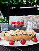 Selbstgebackener Beerenkuchen mit Streuseln und frische Erdbeeren auf Schale, im Freien