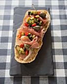 A slice of toasted bread with raw ham, vegetables and capers (Spain)