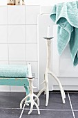 Candlesticks made from branches painted white on grey-tiled floor, turquoise towels on footstool and edge of bathtub