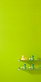 Bunte Badewannen-Enten auf Glasborden vor frühlingsgrün getönter Wand