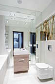 Modernes Bad mit reflektierender Spiegelnische hinter dem Waschtisch; seitlich mit Bambus verstrebte Spiegelfläche über dem WC