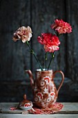 Three carnations in retro-style, painted china coffee pot on doily against dark background