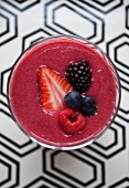 A berry smoothie in a glass on a patterned surface (seen from above)