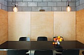 Fruit dish on black dining table in niche with wooden wall panels on concrete block walls