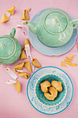 Pastel blue tea crockery, a teapot and broken fortune cookies on a pink tablecloth