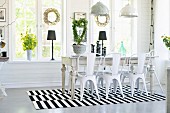 Retro metal chairs around rustic dining table on black and white striped rug below pendant lamps in dining room with wreaths on windows