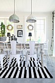 Retro metal chairs at rustic dining table on black and white striped rug below pendant lamps with metal lampshades