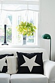 Black cushion with white star motif on white sofa next to standard lamp