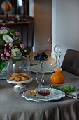 Pastries under glass cover and glass carafe of juice with spherical stopper on set table