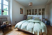 Doppelbett mit lindgrüner Bettwäsche in schlichtem Schlafzimmer, im Hintergrund Einbauschrank mit Sprossentüren